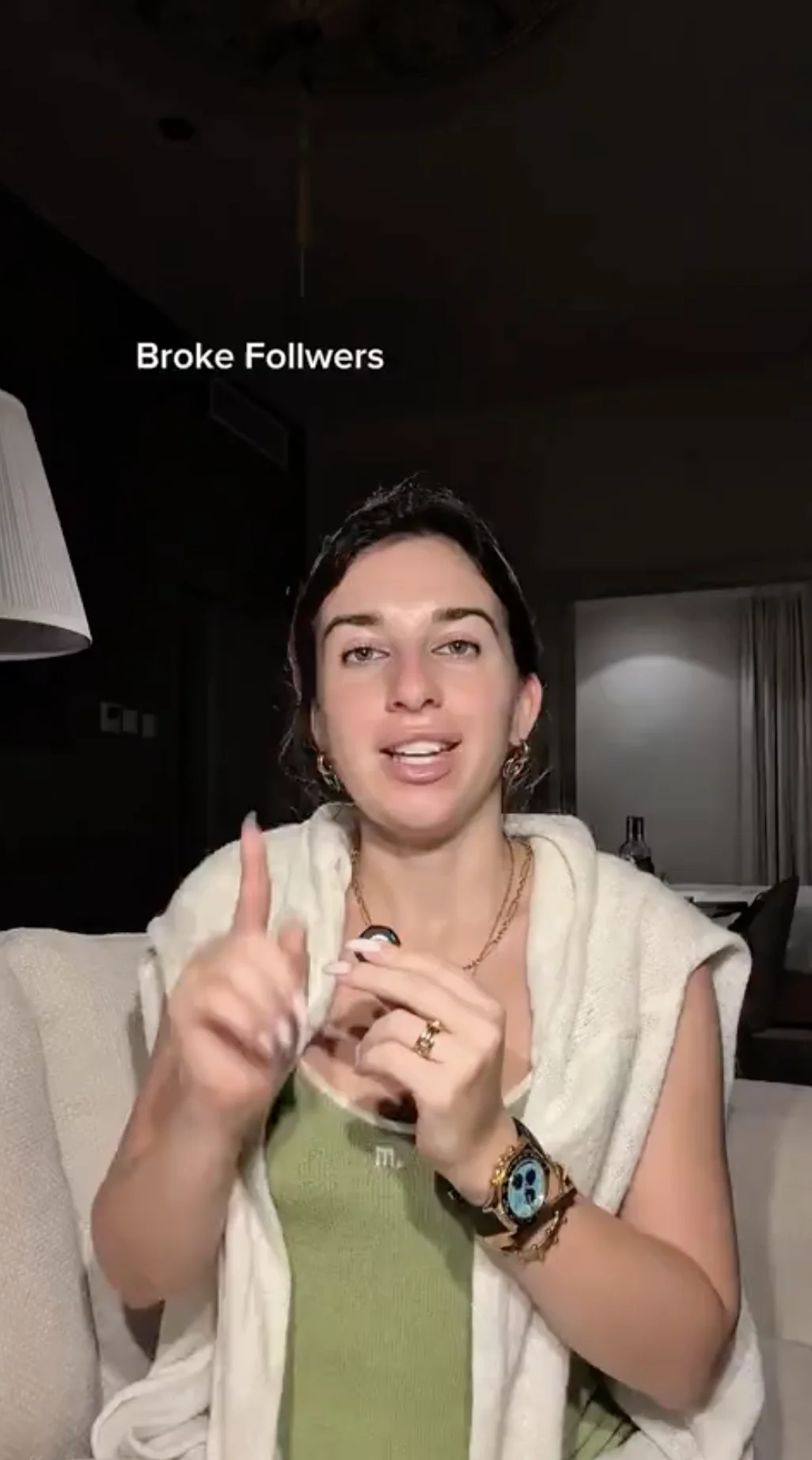 Vertical opening frame from personalbrand_baddie's 49-second video: the "Broke Followers" title over the speaker gesturing on a couch in a dim, lived-in room with a lamp and curtained doorway behind her.