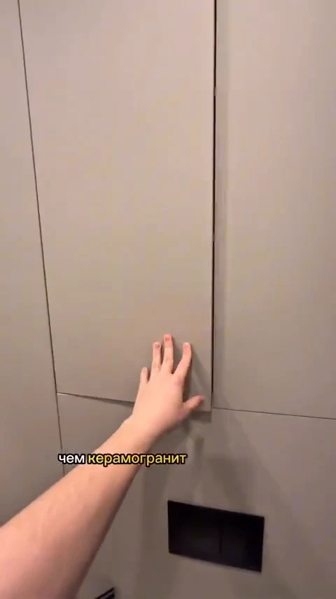 A hand presses flat against a large-format beige wall panel with a concealed dark access hatch below it, captioned in Russian "than porcelain stoneware" (чем керамогранит).