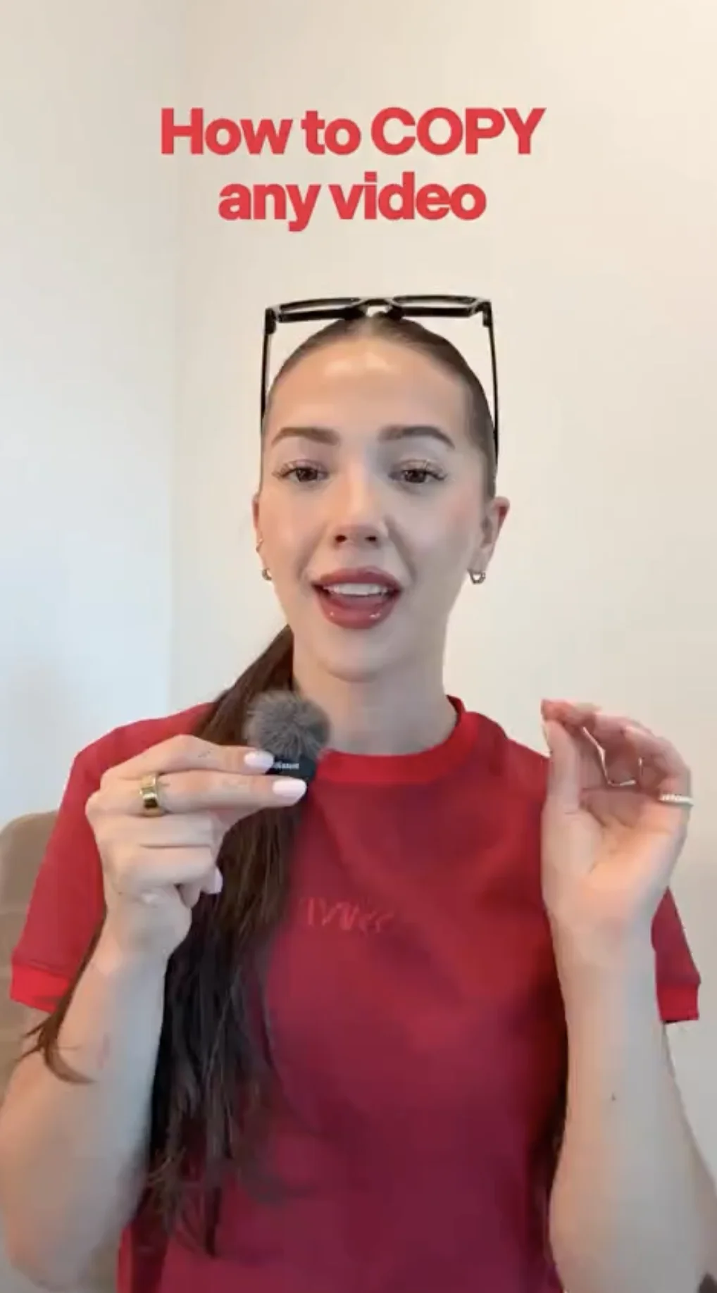 Vertical opening frame from itsashleyboston's tutorial. The same headline "How to COPY any video" in red sits above the creator in a red shirt holding a lavalier microphone, the frame that produced the strongest measured wow reaction of either video.