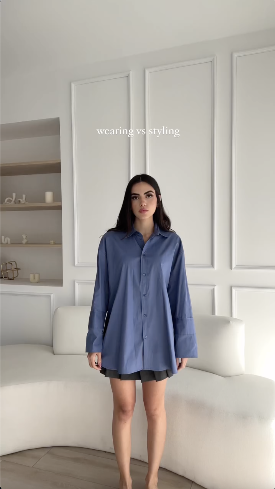 Vertical screenshot from the 5M-view "wearing vs styling" video. A woman in an oversized blue button-down shirt over a grey skirt, with the "wearing vs styling" title set in small serif at the top.